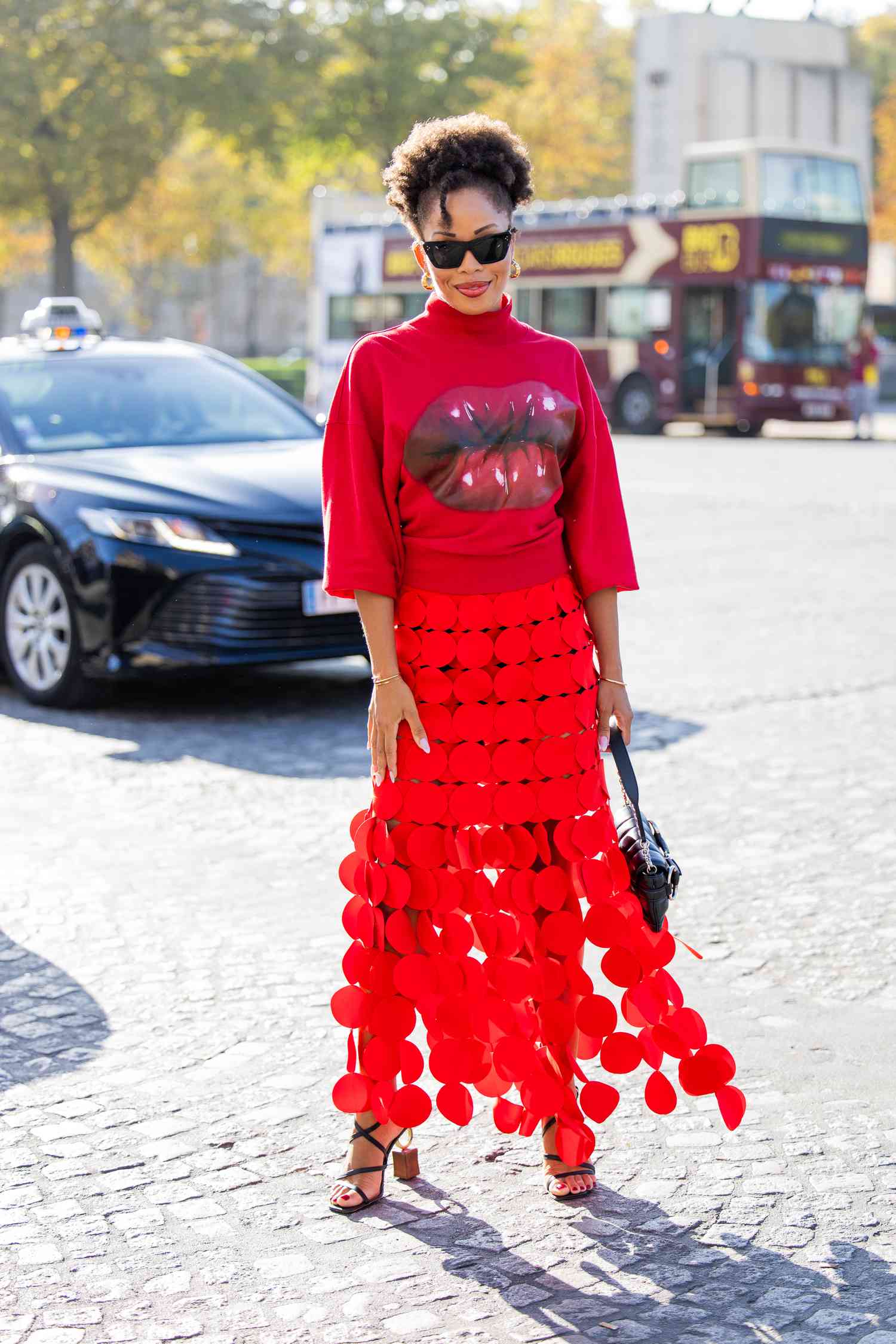 Person with curly hair in an updo wears a red turtleneck and red skirt with black heels