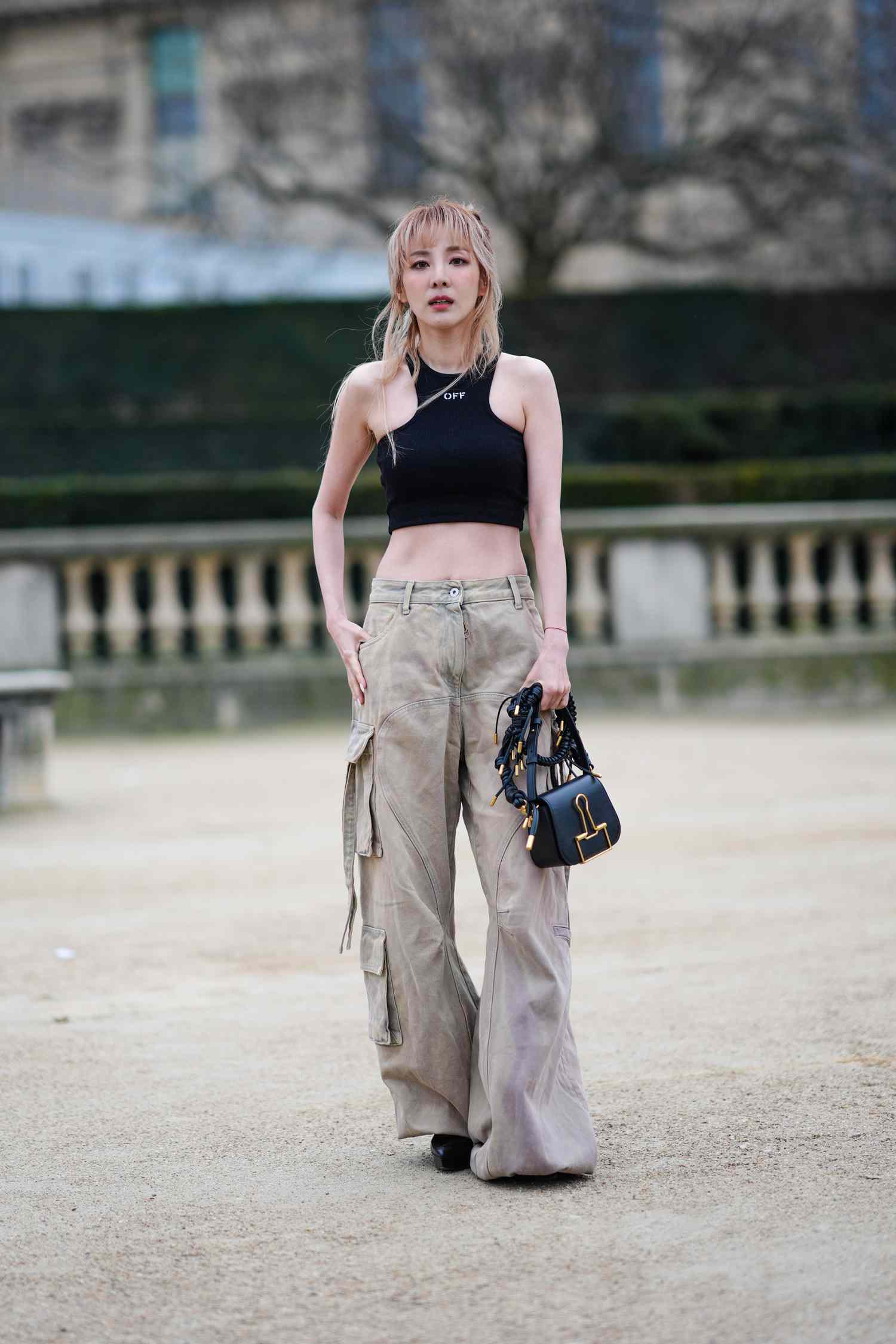 Blonde person wearing a black crop top and khaki wide-leg pants holding a black purse