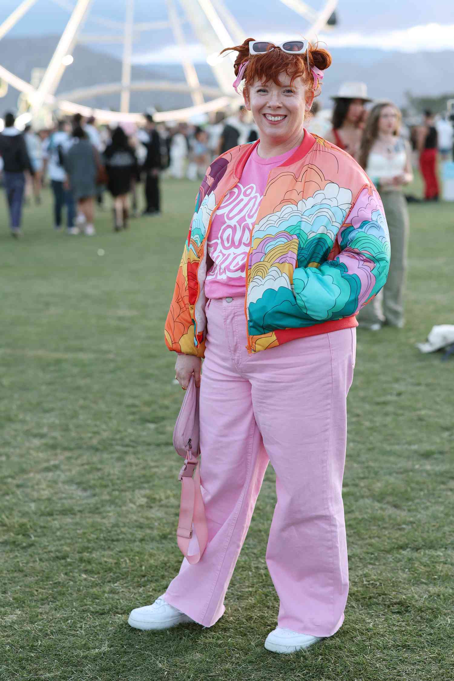 Person with red hair in space buns wears a colorful jacket over a pink shirt and pink pants