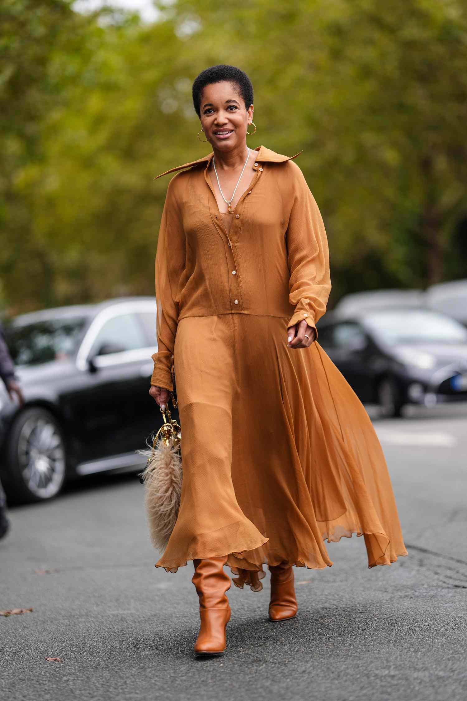 Person with short, coily hair wears a flowy, long-sleeve camel-colored dress with matching boots