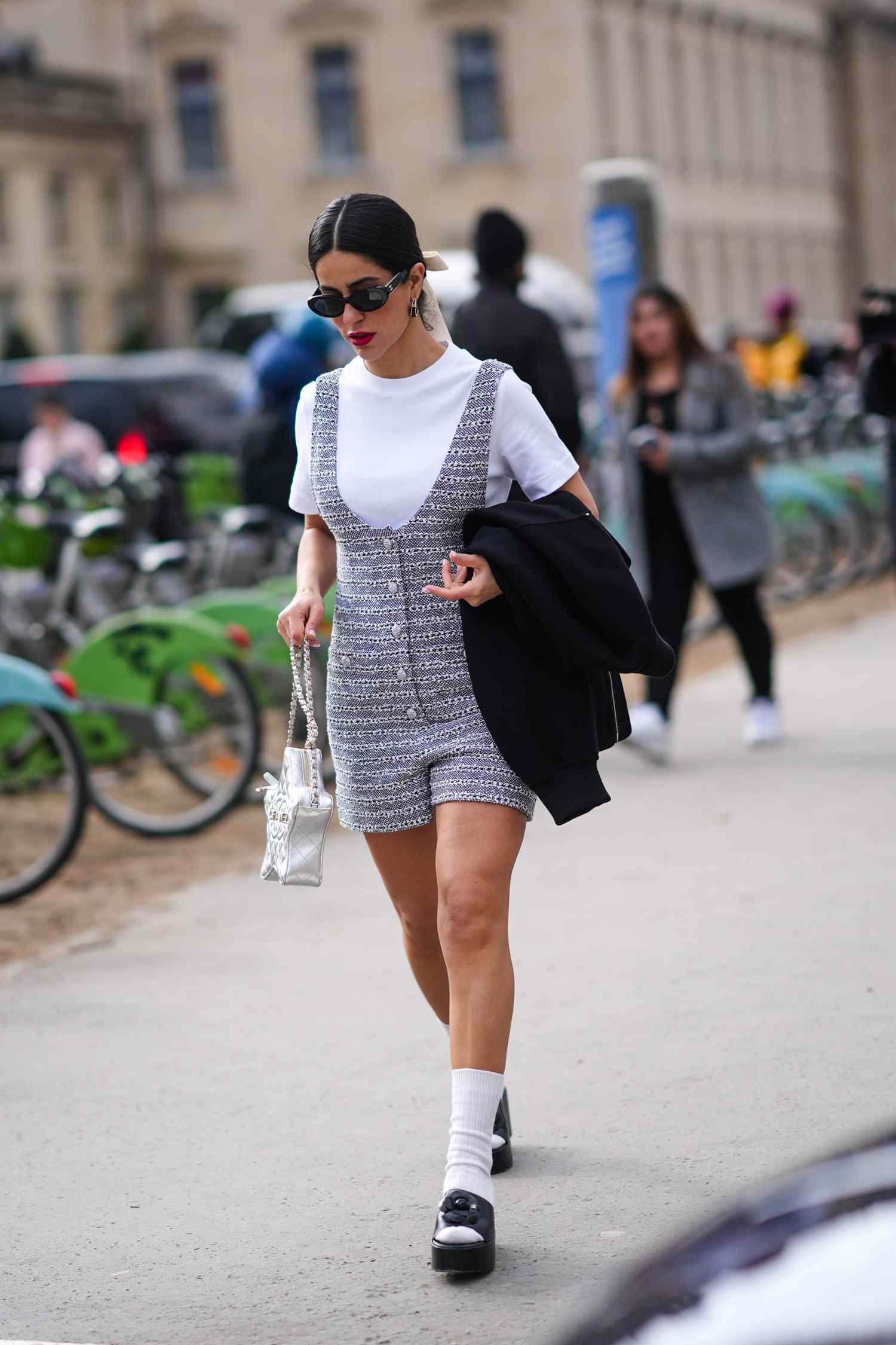 Person with their dark hair in a bun while wearing a short jumpsuit over a white tee