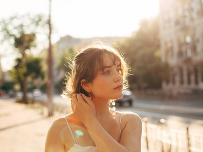 A woman standing outdoors on a sunny day touching her earring