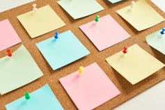 A corkboard with different coloured squares of paper attached to it with push pins.