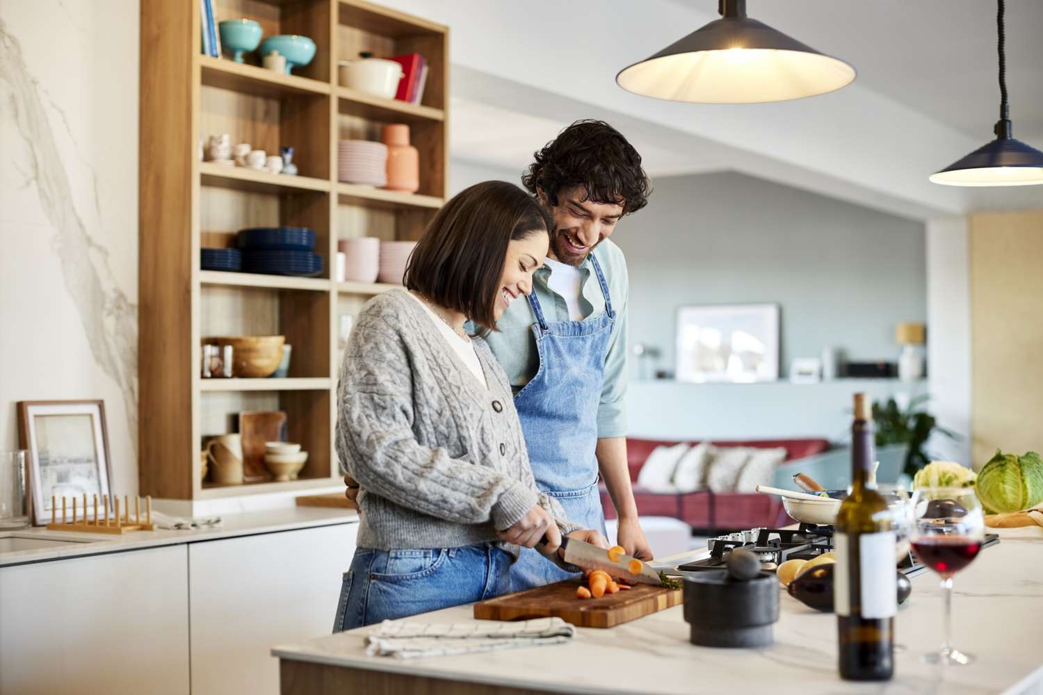 Smiling man looking at woman chopping carrot. Happy couple is cooking food together at home. They are in kitchen.