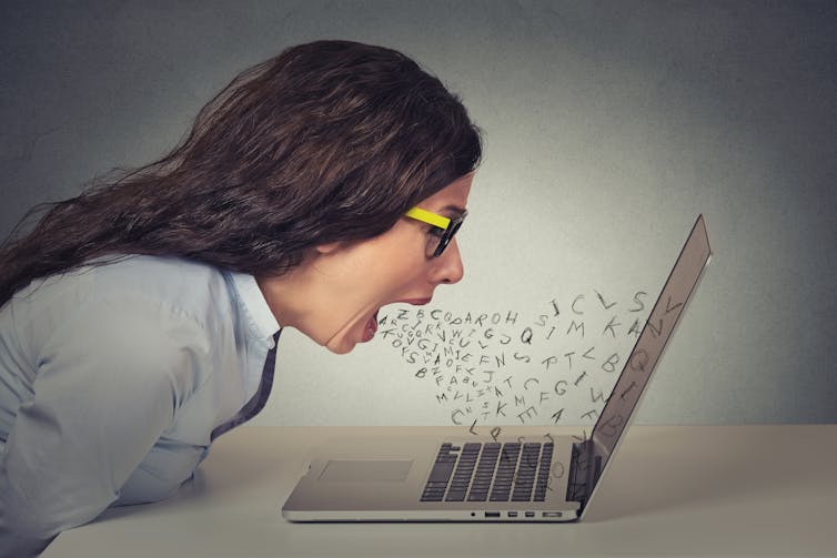 Angry furious businesswoman working on computer, screaming with alphabet letter coming out of open mouth