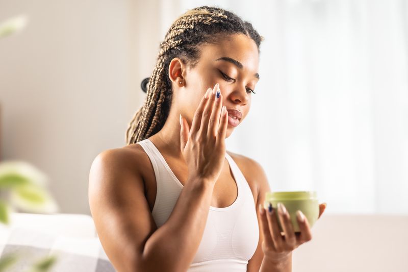 Person applying moisturizer to their face while holding a container