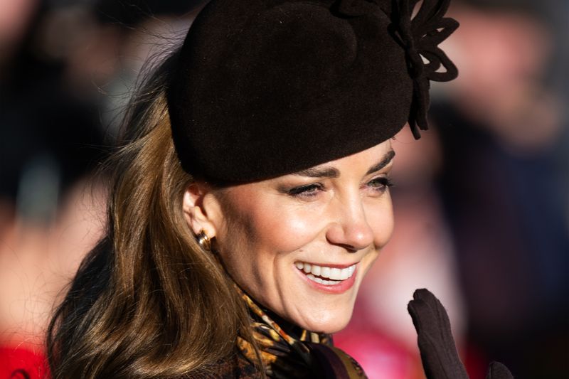 A woman smiling and wearing a hat waving outdoors in a candid setting