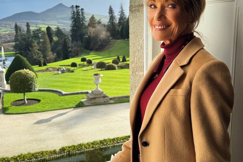 Jane Seymour standing indoors near a window overlooking a landscaped garden