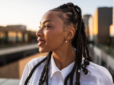 A person looking to the side with braided hair and a white shirt standing outdoors