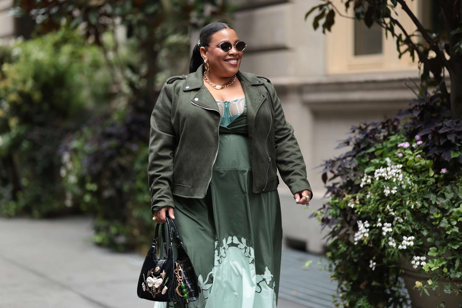 Person walking along a sidewalk wearing sunglasses and holding a handbag