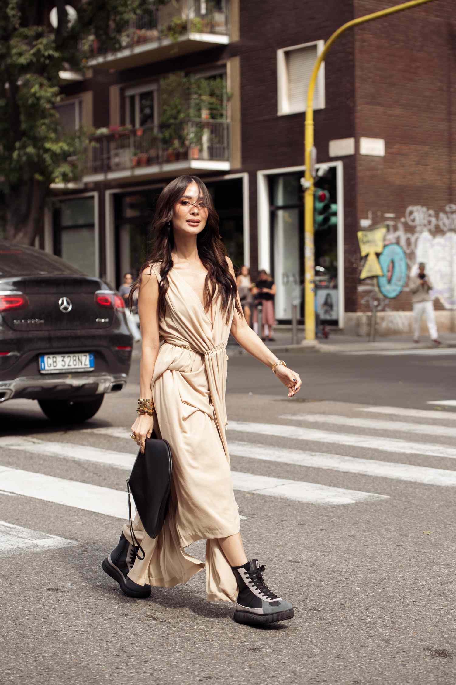 A woman crossing a street wearing a light loose outfit and carrying a black bag