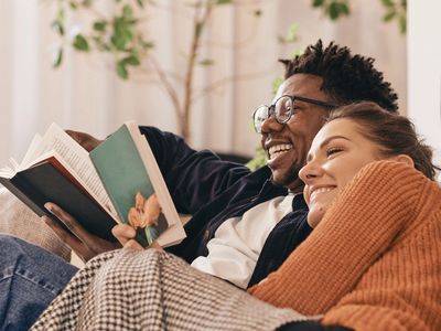 Happy couple in cozy sweaters cuddle up to read their own books