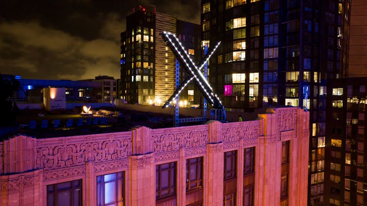 Workers install a large illuminated X on top of a building at night.